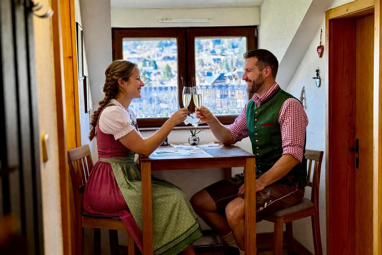 Heli's Holiday Suites | Ferienwohnung Balkon-Trisselwand - A bright living room featuring a large wooden wardrobe and a TV. Two green armchairs are placed around a coffee table. Sunlight streams across the wooden floor and a striped rug. Sheer curtains cover a large window, and a balcony door offers a glimpse of the outdoors. The atmosphere is warm and inviting.